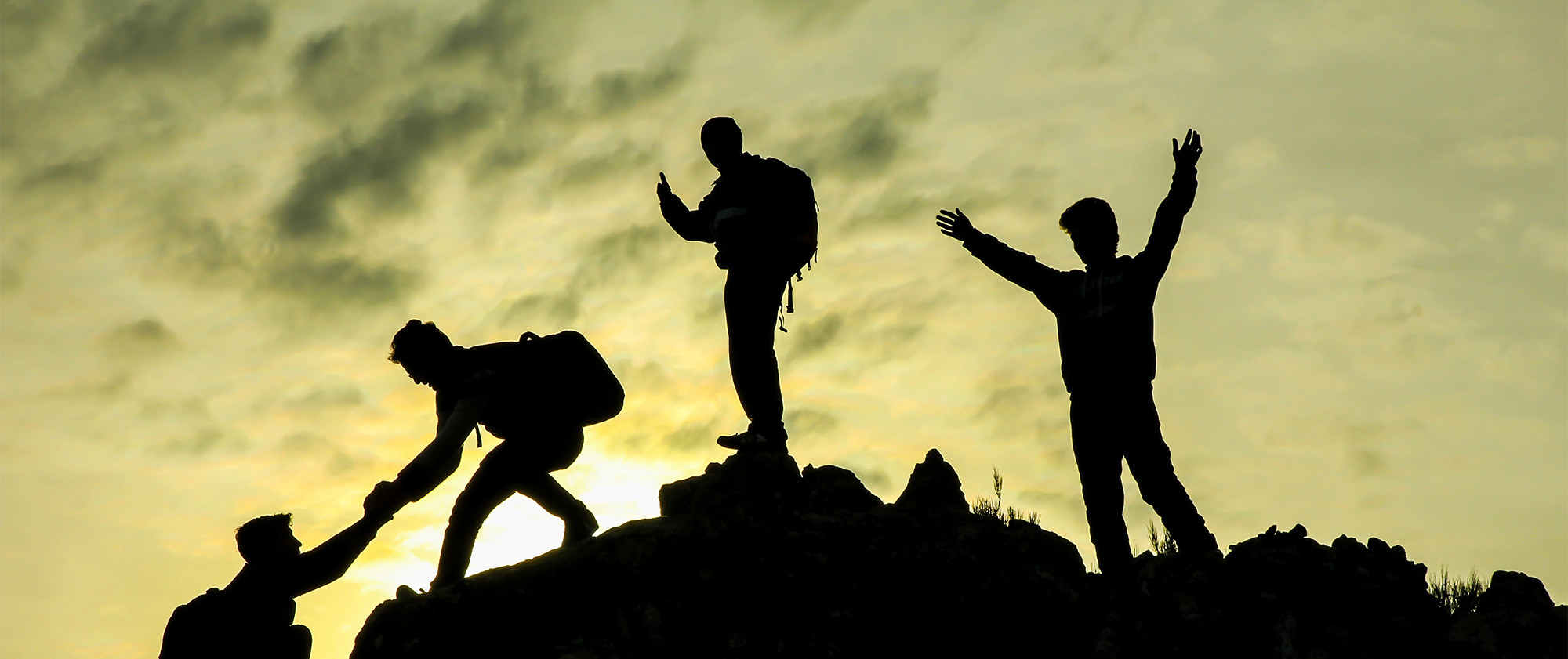 Bergsteiger helfen einander auf einen Berggipfel vor Sonnenuntergang.